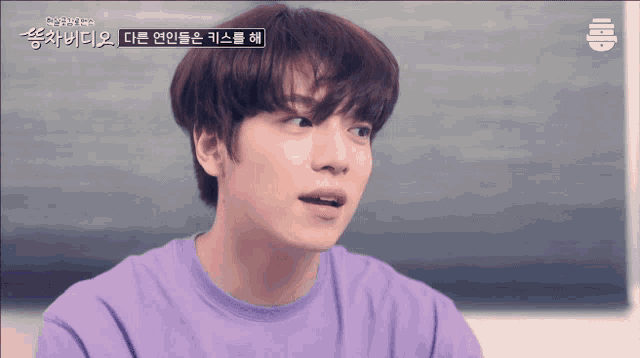 a young man in a purple shirt is sitting in front of a blackboard with chinese writing on it