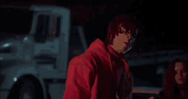 a man in a red jacket is standing in front of a white truck and a woman .