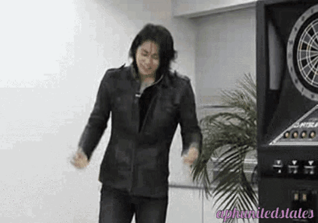 a man in a leather jacket is standing in front of a dart board .