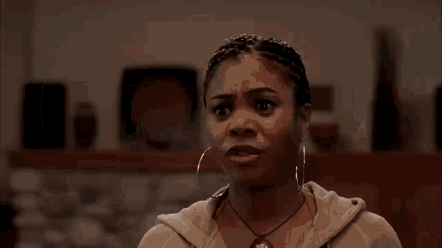 a woman wearing a hoodie and hoop earrings is making a funny face .