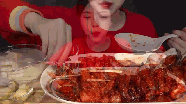 a woman in a red shirt is eating a large plate of food with a spoon