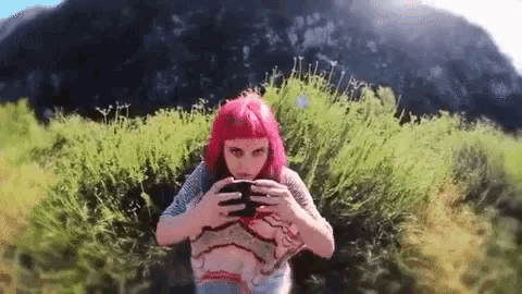 a woman with pink hair is taking a picture of herself in a field .