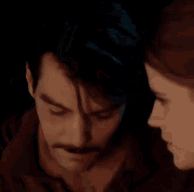 a man with a mustache is kissing a woman on the forehead .