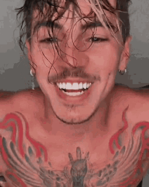 a shirtless man with a tattoo on his chest is smiling and looking at the camera .