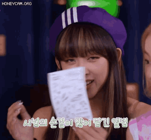 a woman wearing a purple hat is holding a piece of paper in her hands .