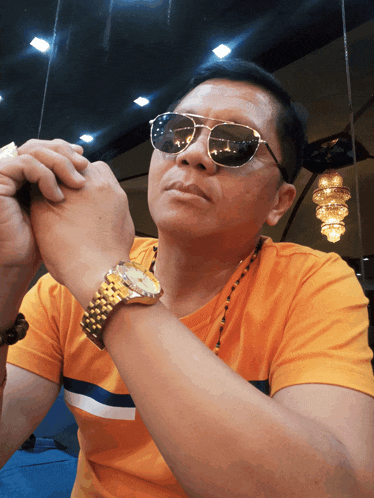 a man wearing sunglasses and a gold watch looks to his left