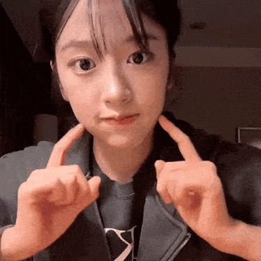 a young woman is making a face with her hands while wearing a black jacket