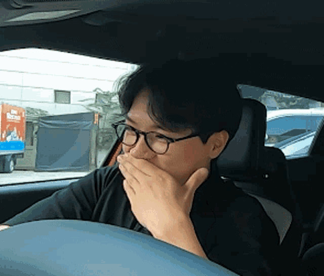 a man wearing glasses is sitting in a car covering his mouth