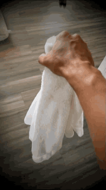 a hand holding a white towel on a wooden floor
