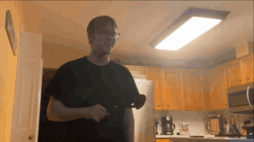 a man in a black shirt is standing in a kitchen near a refrigerator
