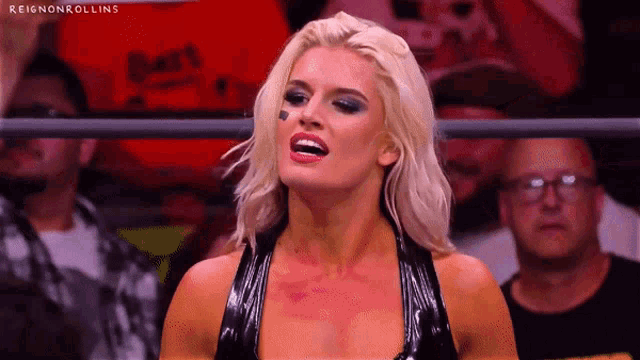 a woman in a black dress is standing in a ring with a crowd behind her .