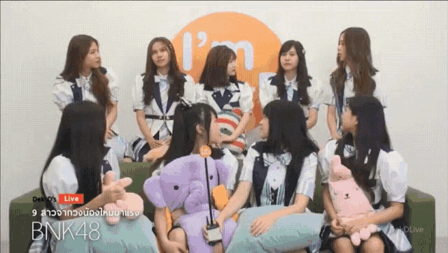 a group of girls are sitting in front of a sign that says " i 'm bnk48 "