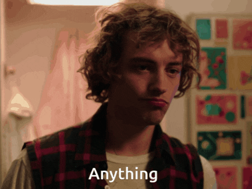 a man with curly hair is wearing a plaid vest and has the word anything written on his face