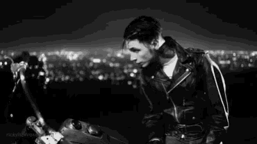 a man with a tattoo on his neck is wearing a leather jacket and looking at the camera .