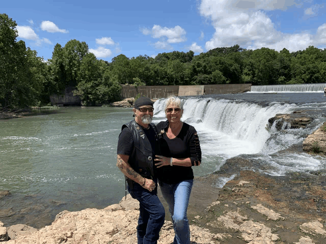 a man and a woman are posing for a picture in front of a waterfall