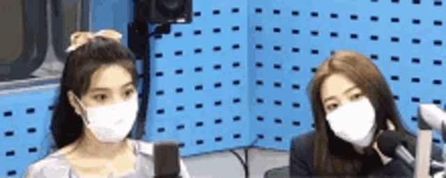 two women wearing masks are talking into microphones in a radio studio .