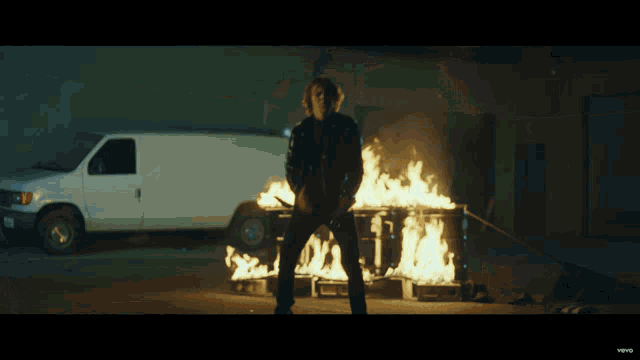 a person standing in front of a burning trash can with a white van in the background