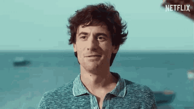 a man in a blue shirt is smiling in front of the ocean with a netflix logo in the background