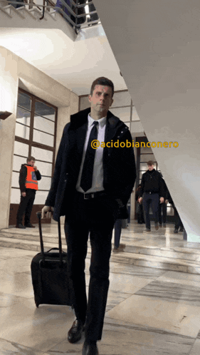 a man in a suit and tie is walking with a suitcase in front of a sign that says acidobianconero