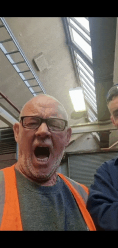 a man wearing glasses and an orange vest is making a funny face with his mouth open