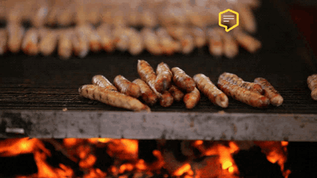 a bunch of sausages are cooking on a grill with a yellow speech bubble that says ' e '
