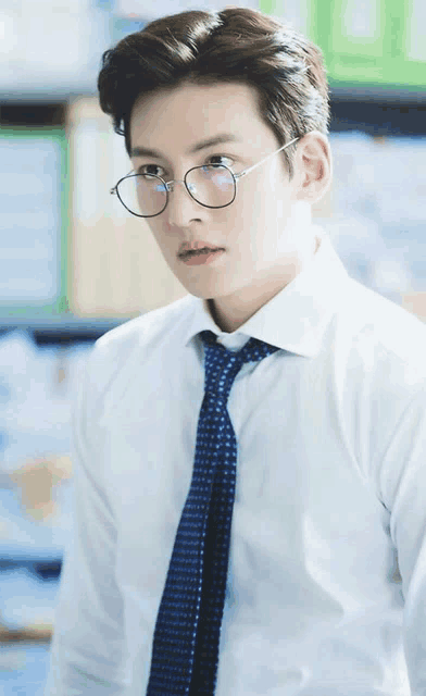 a man wearing glasses and a blue tie looks at the camera