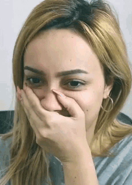 a woman is covering her mouth with her hand and making a funny face .