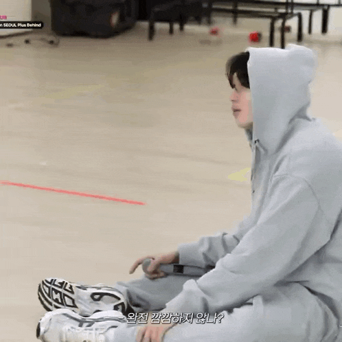 a man in a hoodie is sitting on the floor with his legs crossed .