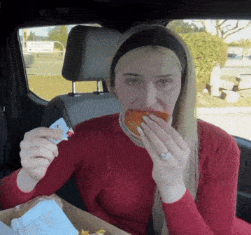 a woman in a red sweater eating a hamburger