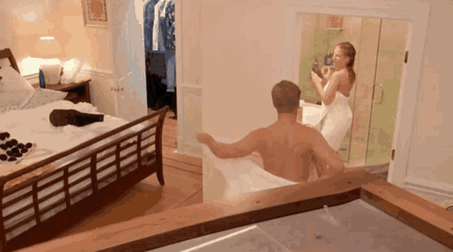 a man and a woman wrapped in towels are standing in a bedroom .