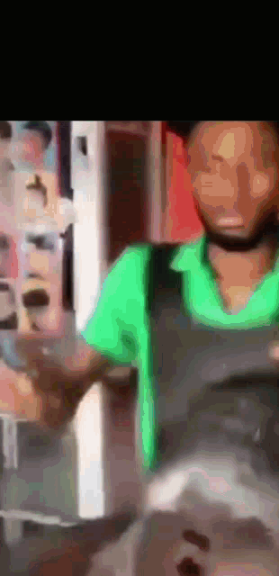 a man in a green shirt and black apron is standing in front of a refrigerator