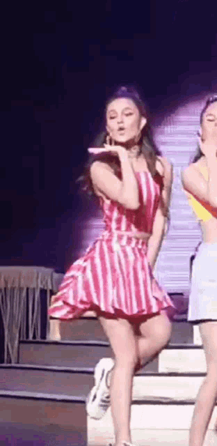 a woman in a red and white striped dress is standing on a stage with a microphone .