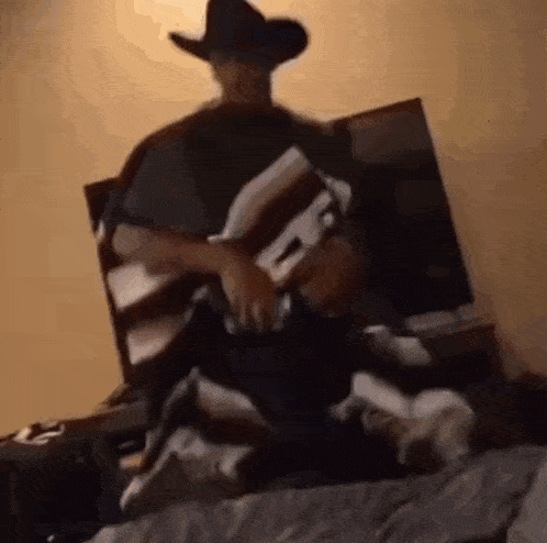 a man in a cowboy hat and poncho is sitting on a bed .