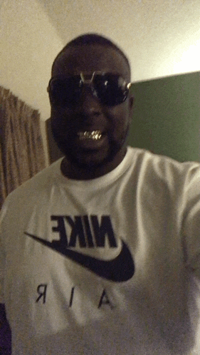 a man wearing sunglasses and a white nike shirt takes a selfie