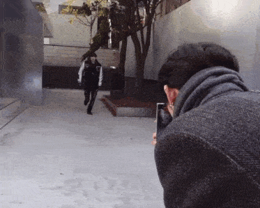 a man taking a picture of another man walking down a sidewalk