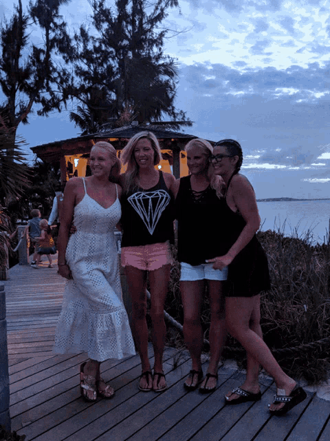 four women are posing for a picture with one wearing a diamond tank top