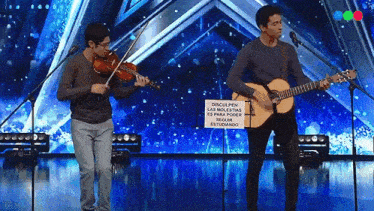 two men playing violins and guitars on a stage with a sign that says " disculpen las molestias "