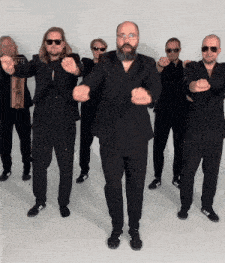 a group of men in black suits and sunglasses are dancing together