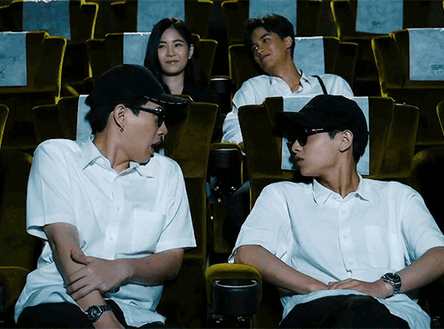 a group of people are sitting in a theater watching a movie and one of them is wearing sunglasses