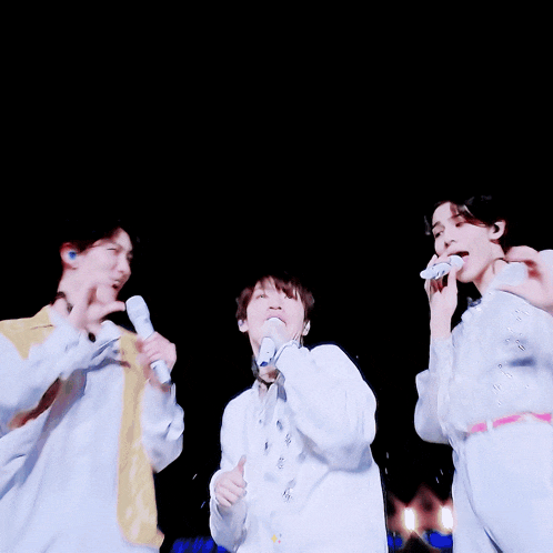 a man in a white shirt is holding a microphone and making a heart with his hands