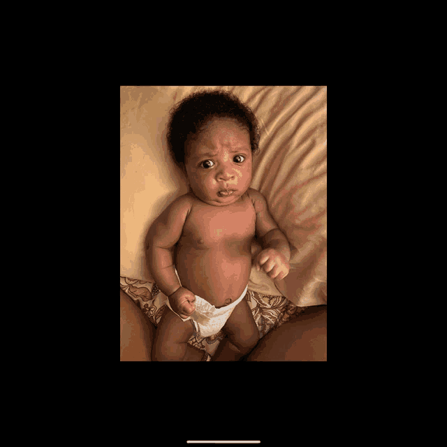 a baby in a diaper laying on a bed looking at the camera