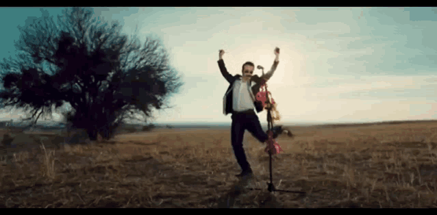 a man is standing on a microphone in a field with his arms up .