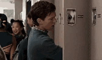 a young man is standing in front of a locker in a hallway .