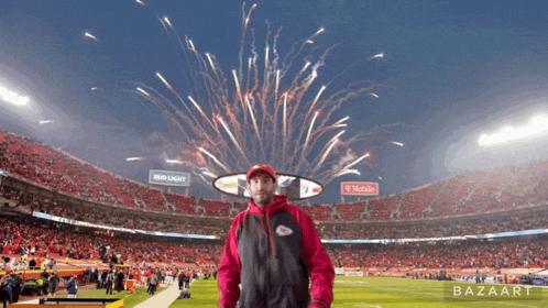 a man stands in front of a fireworks display in a stadium sponsored by bud light