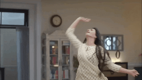 a woman in a white dress is dancing in a living room with her arms outstretched and her hair blowing in the wind .