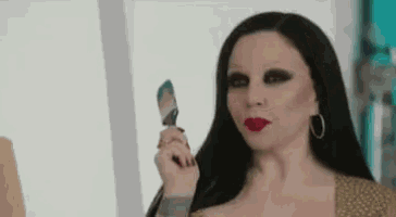 a woman with long black hair and red lips is holding a spatula in her hand .