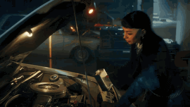 a woman looking under the hood of a car with the hood open