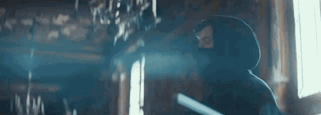 a man in a hooded sweatshirt is standing in a dark room holding a sword .