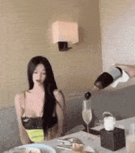 a woman is sitting at a table with a bottle of champagne being poured into her glass .