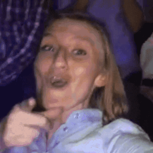 a woman in a blue shirt is making a funny face while pointing at the camera .